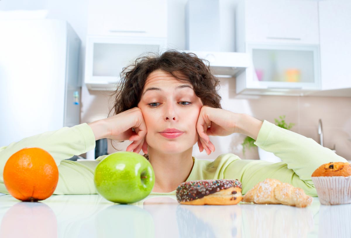 Woman choosing between an apple and a cupcake